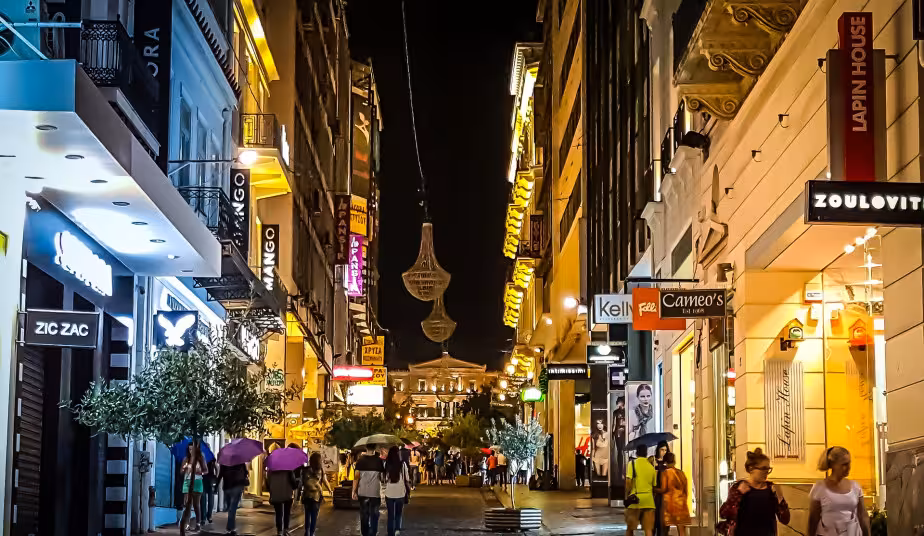Athens night street with glowing shopfronts and crowds, ideal for guided food tour tasting gyros and loukoumades