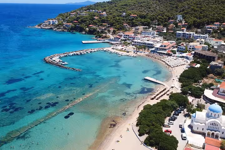 Aerial view of a Saronic Gulf island beach stop on Athens all-day cruise, clear water bay and seaside village