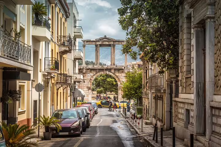 Narrow Athens street leading to Hadrian's Arch with parked cars and neoclassical buildings