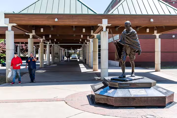 Gandhi statue at Atlanta plaza with two visitors walking under covered colonnade