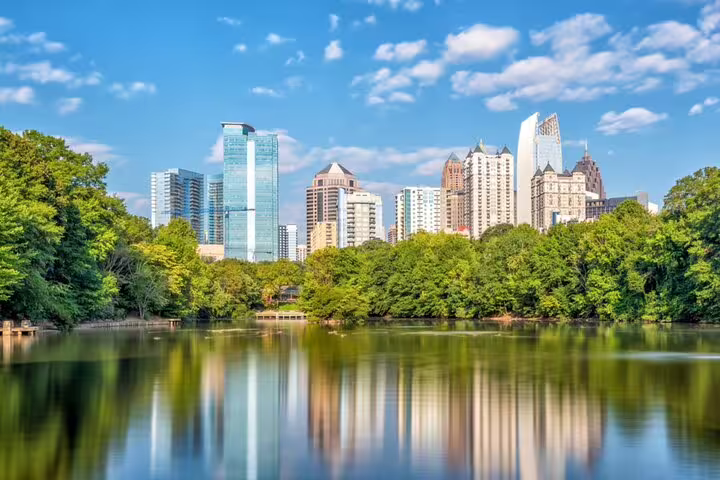 Atlanta skyline reflected in Piedmont Park lake surrounded by lush green trees on a sunny day