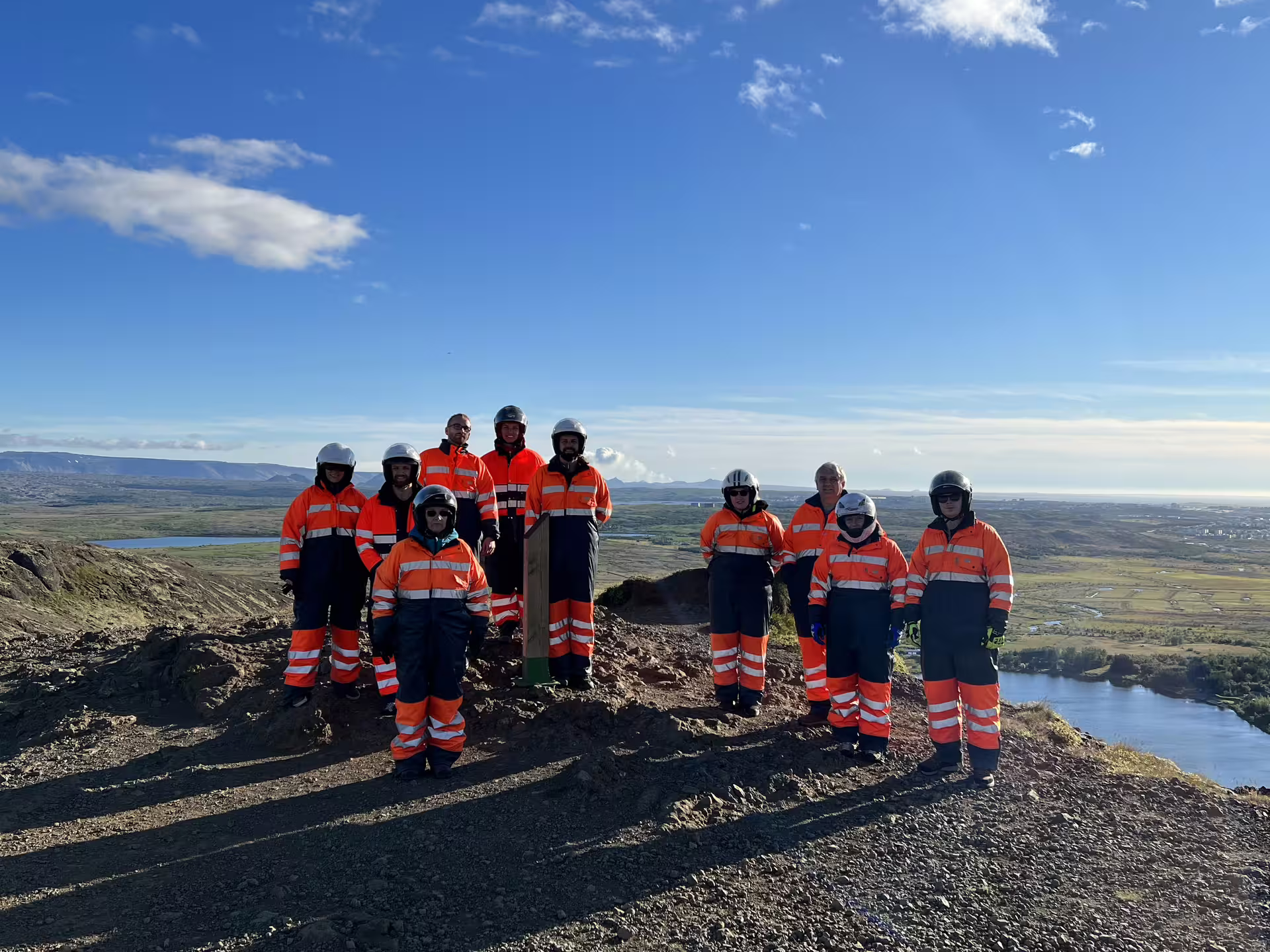 Group in orange safety suits and helmets on volcanic hilltop overlooking Reykjavik landscape on ATV tour