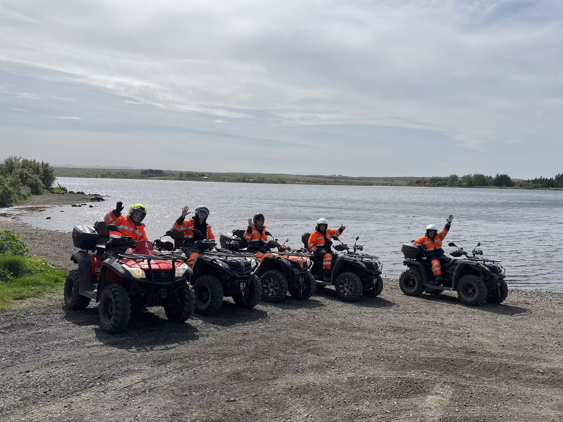 Group of riders in orange safety gear on ATVs lined up along a scenic riverbank in Reykjavik
