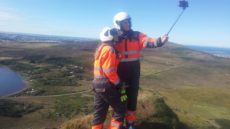 Two people in helmets and hi-vis suits taking a selfie on an ATV tour with panoramic Reykjavik views