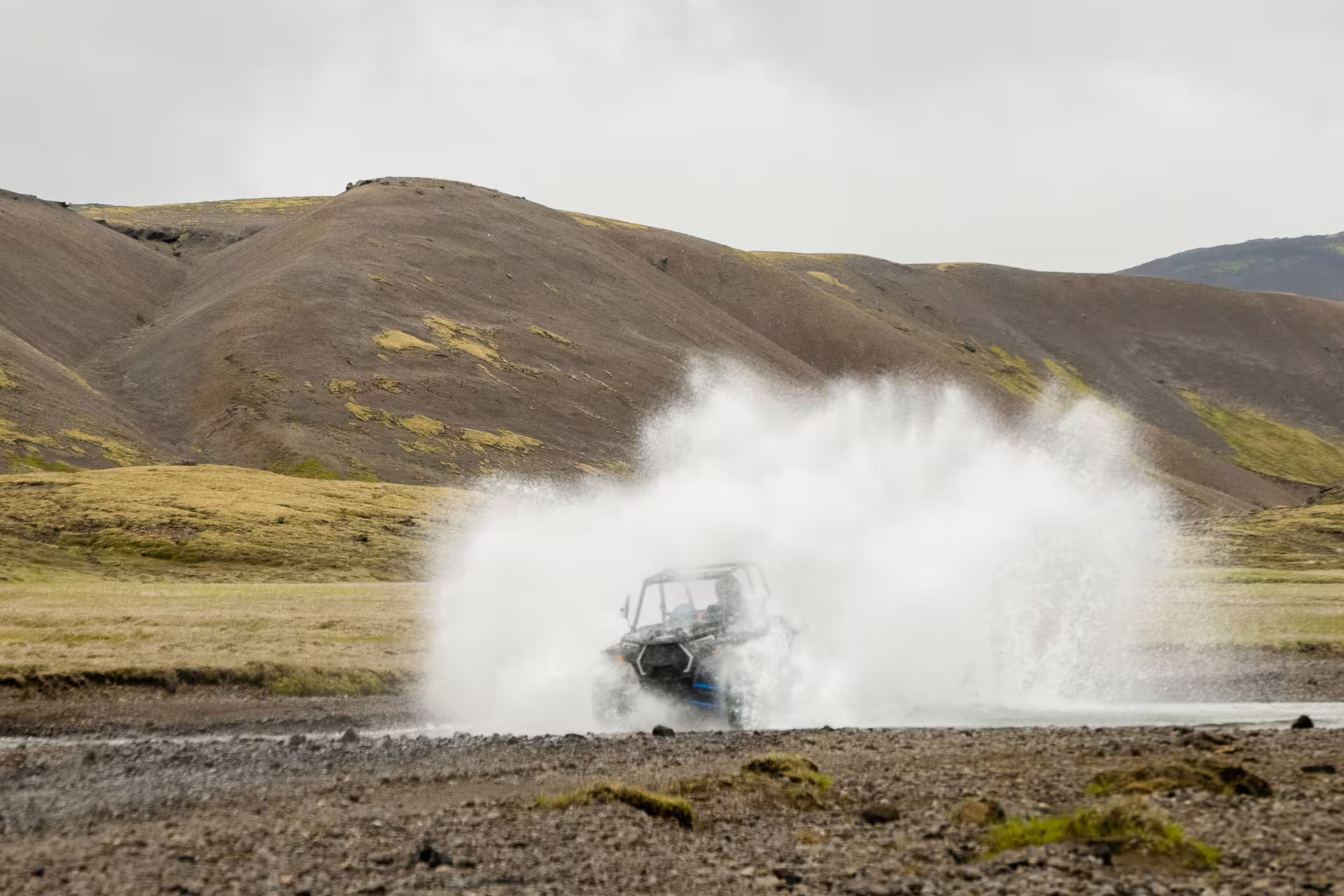 ATV buggy splashing through a river crossing with dramatic Icelandic highland scenery in the background