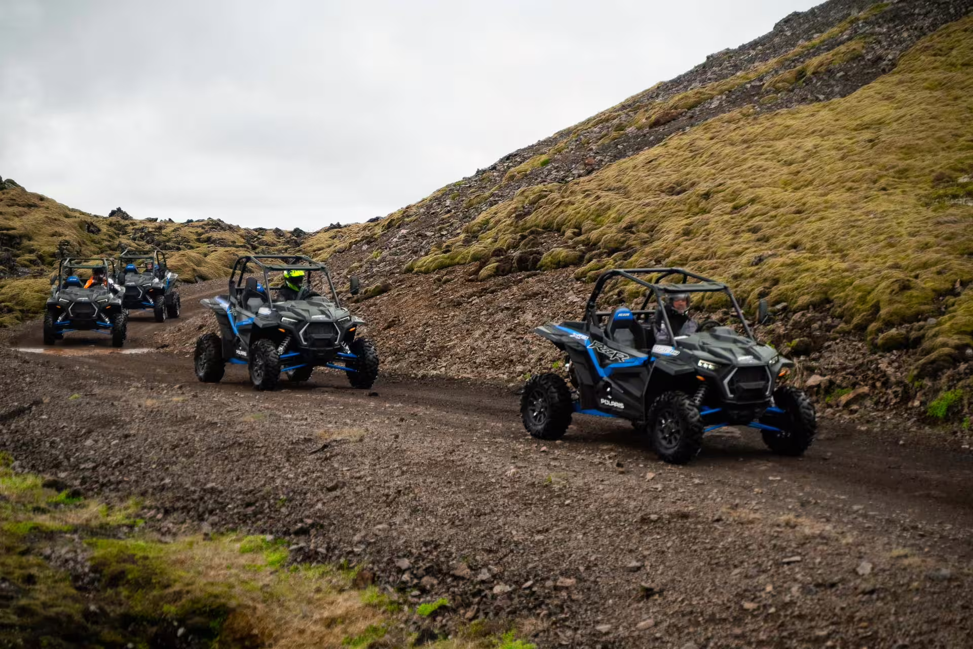 Group of Polaris RZR buggy ATVs driving on a rocky dirt trail through mossy lava fields in Iceland