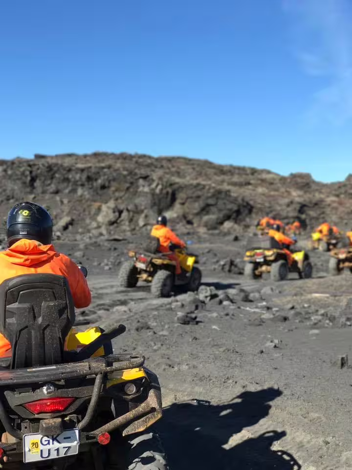 Group of ATV riders in orange jackets traversing black lava fields on Iceland's black sand beach trail