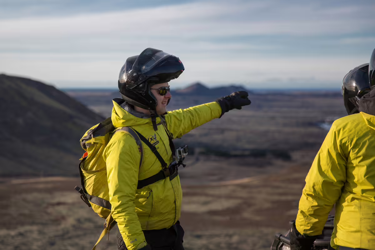 Tour guide in yellow jacket and helmet pointing at volcanic Iceland landscape during ATV lava trail tour
