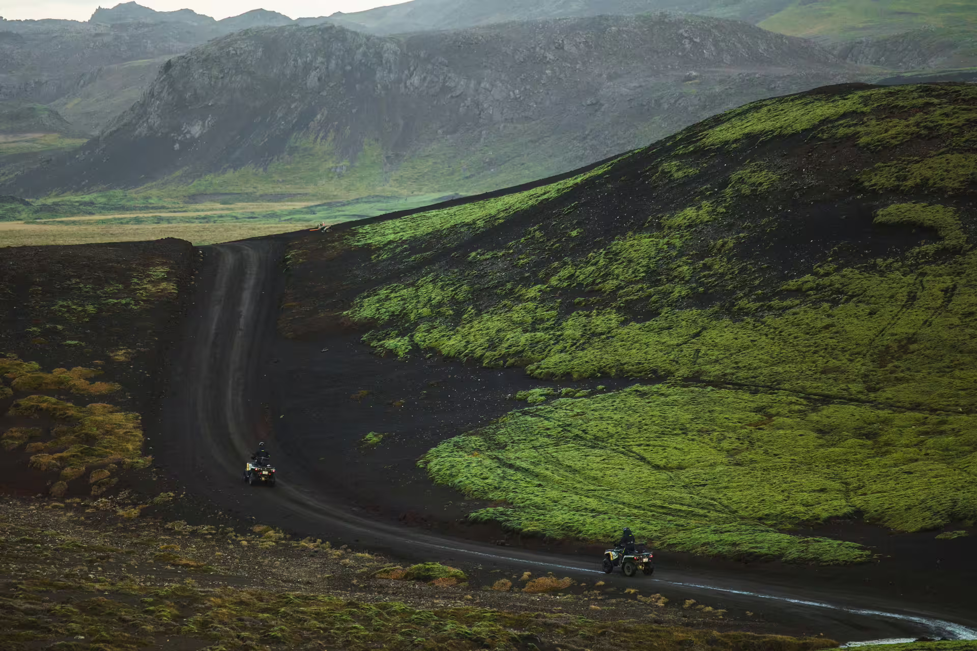 Two ATVs riding on black volcanic trail through green moss-covered lava fields in Iceland