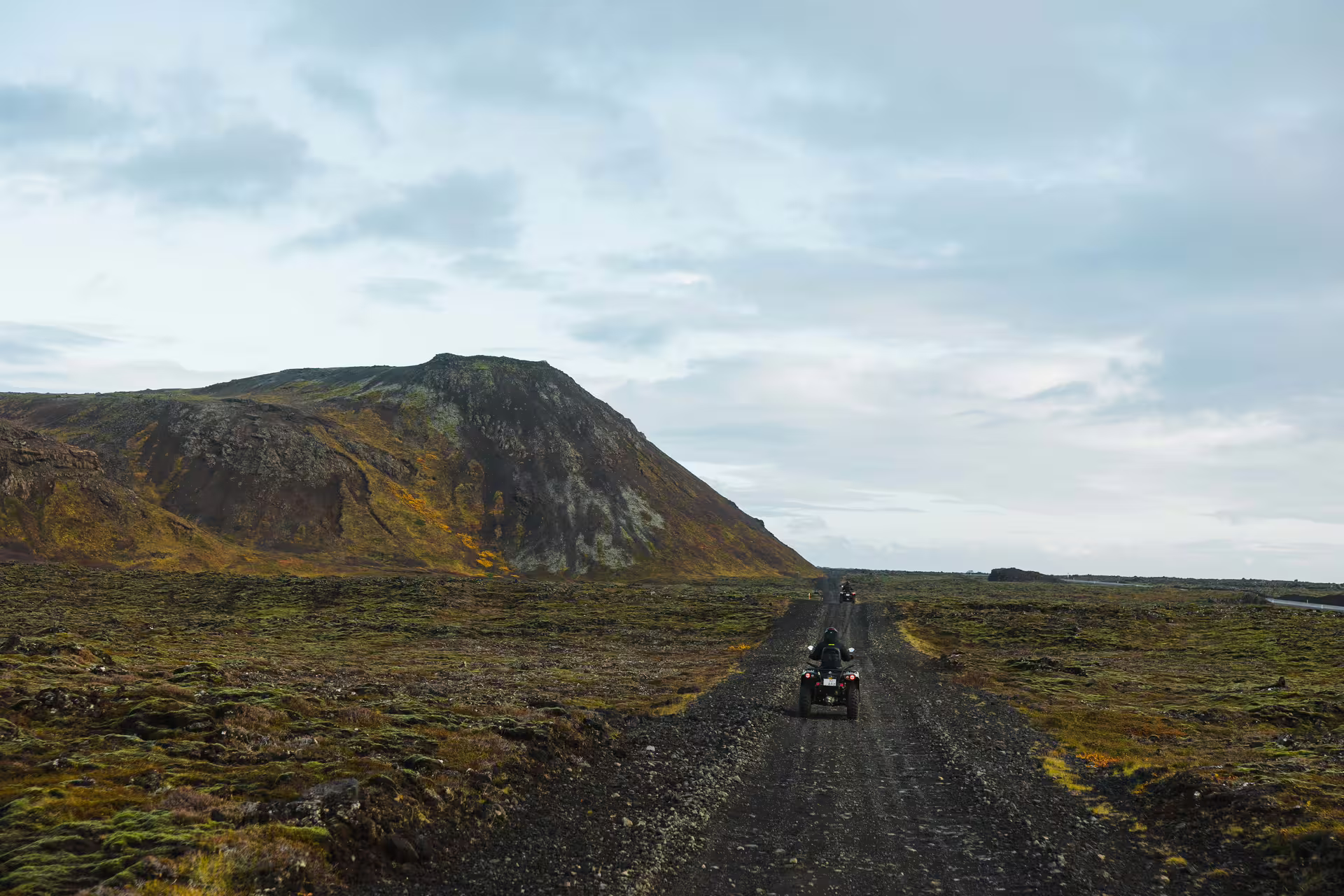 ATV riders on a gravel trail through Iceland's volcanic lava fields with a rugged mountain backdrop