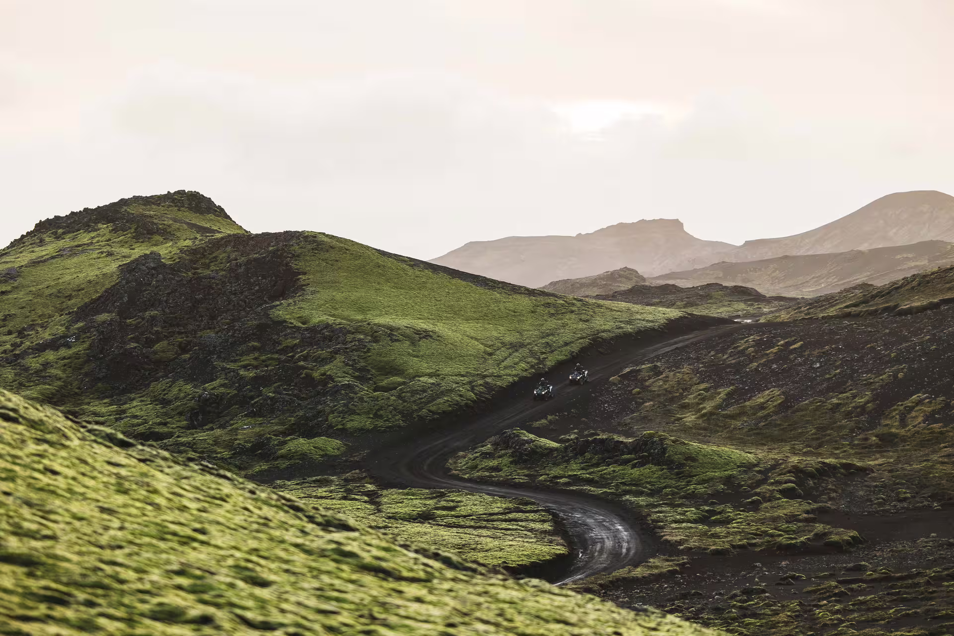 ATVs riding on winding black lava trail through mossy green hills in Iceland highlands