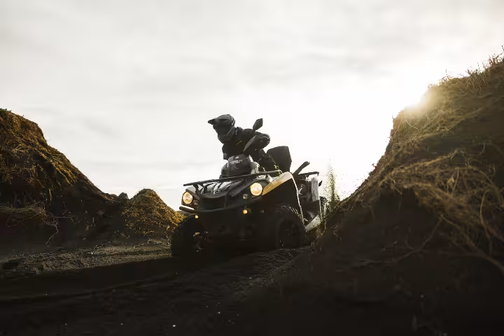 Rider on ATV quad bike navigating black lava trail between dark rocky mounds in Iceland