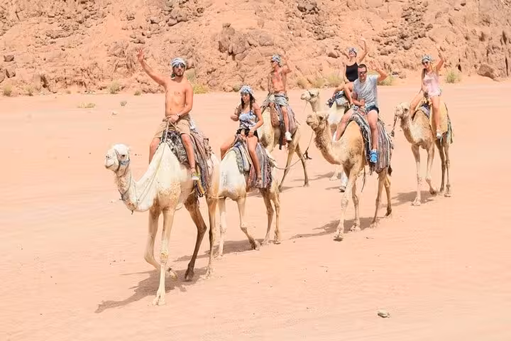 Travelers on camel ride in Hurghada desert during ATV quad bike safari, waving in sandy valley