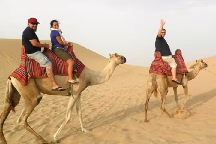 Tourists enjoy a camel ride across Marsa Alam desert dunes on the ATV quad bike safari adventure tour
