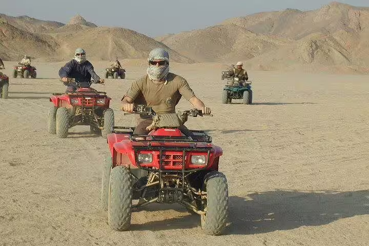 Riders on ATV quad bikes in Hurghada desert safari, wearing scarves and helmets, driving toward rocky hills