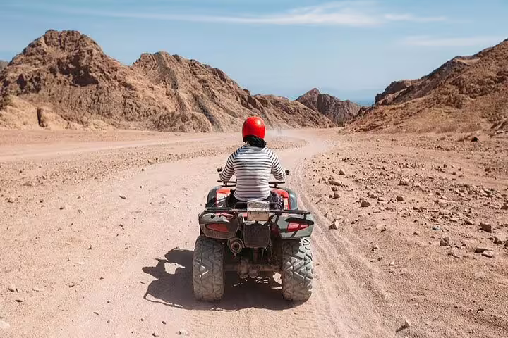 Traveler riding an ATV quad bike in Hurghada desert mountains, part of quad and camel safari with dinner show