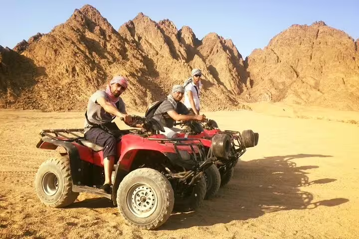 Group on ATV quad bikes near rocky mountains in Marsa Alam desert safari with camel ride and Bedouin dinner