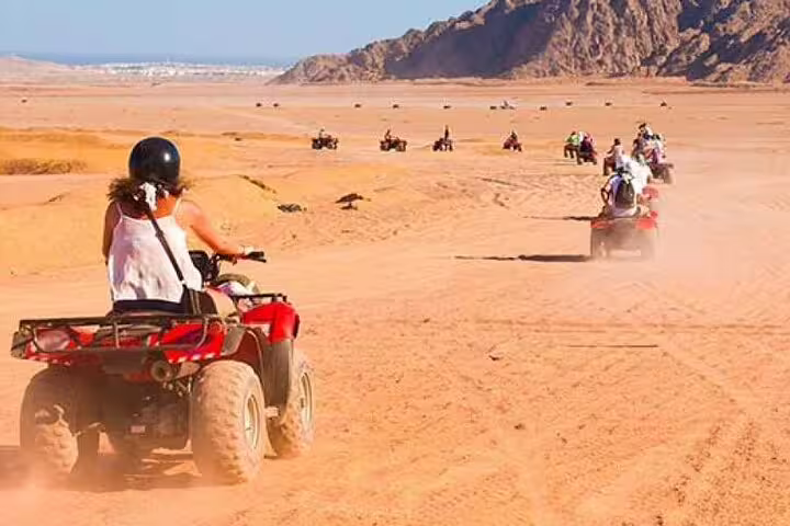 ATV quad bike safari convoy crossing Marsa Alam desert dunes, Red Sea mountains backdrop on adventure tour