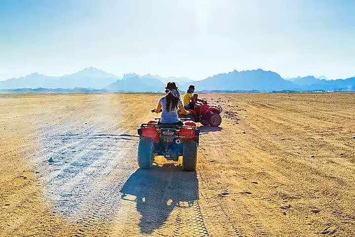 Riders on ATV quad bikes crossing the Hurghada desert safari trail with mountain views and dust tracks