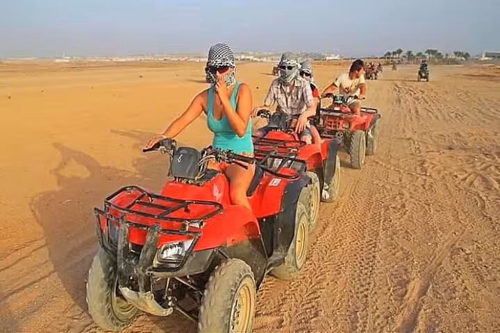 Riders on red quad bikes crossing Hurghada sand dunes on 3-hour ATV quad safari tour before camel ride