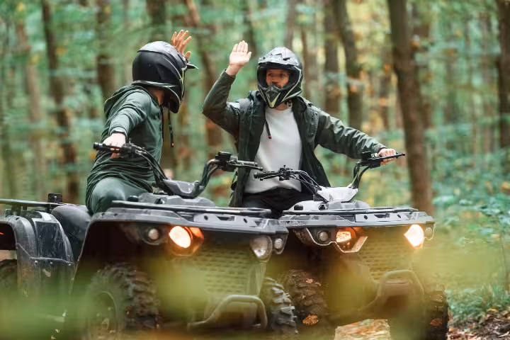 Two riders on ATVs giving high five in forest during quad bike tour