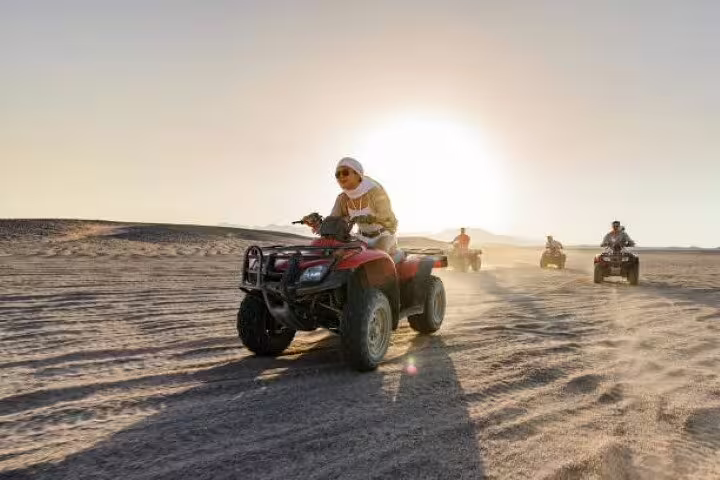 ATV convoy crossing Hurghada desert with dust trails at sunrise, quad bike safari adventure tour and camel ride