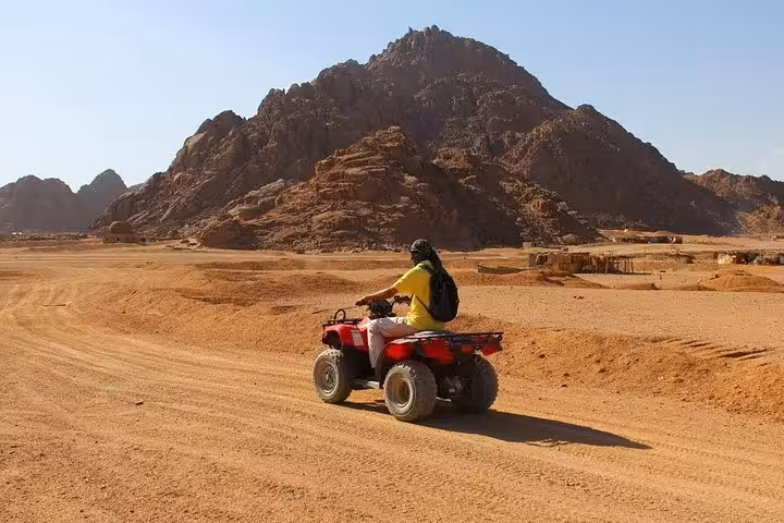 Solo rider on ATV quad bike safari in Sharm El Sheikh, cruising desert trail with rugged Sinai mountains ahead