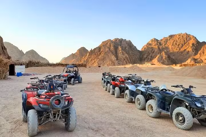 Lined-up ATV quad bikes at Hurghada desert safari base with Red Sea mountains, ready for camel ride tour
