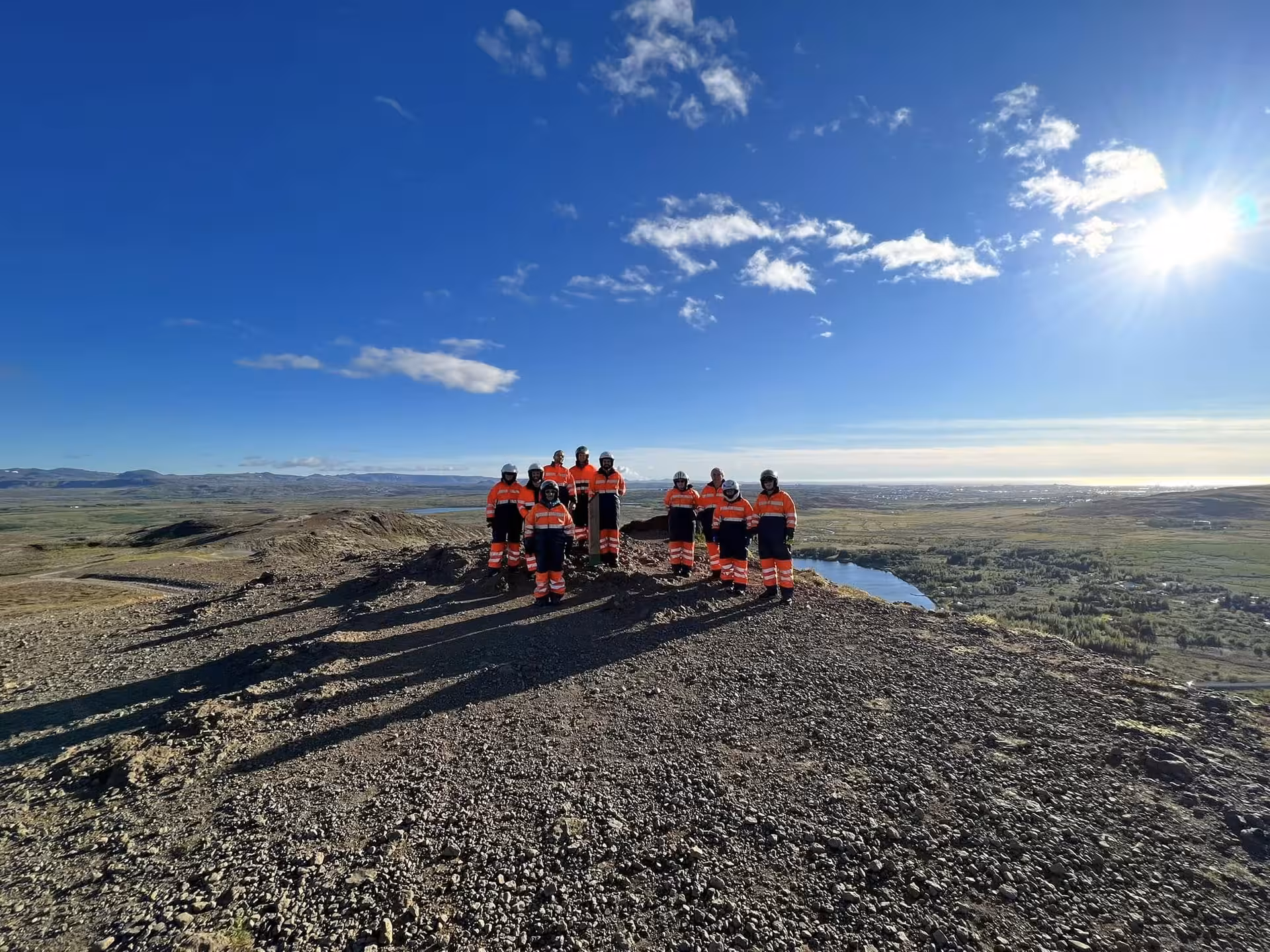 Group in orange safety gear standing on volcanic hilltop with panoramic Iceland wilderness view at sunset