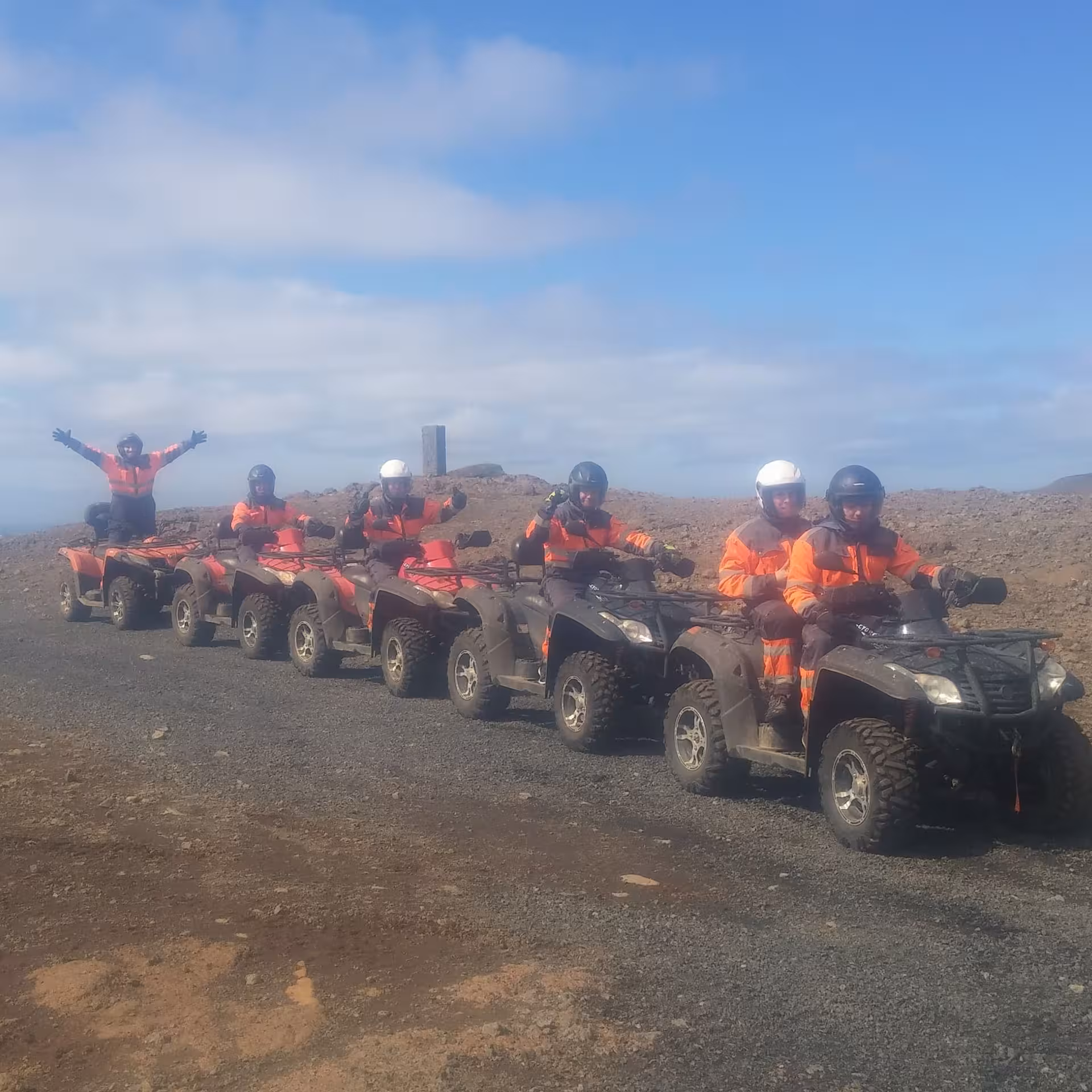 Group of riders in orange suits on ATVs lined up on volcanic terrain near Reykjavik under blue sky
