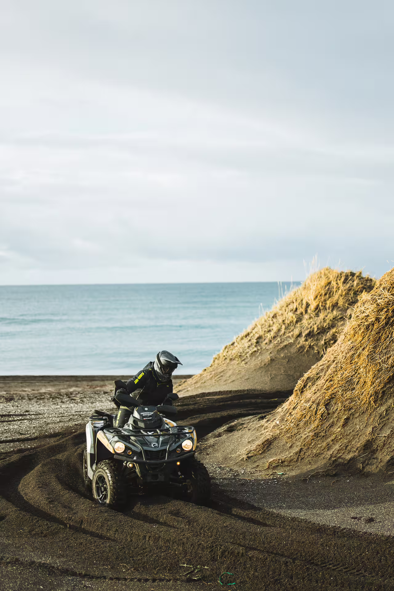 Rider on Can-Am ATV navigating black sand dunes near ocean coastline in Iceland