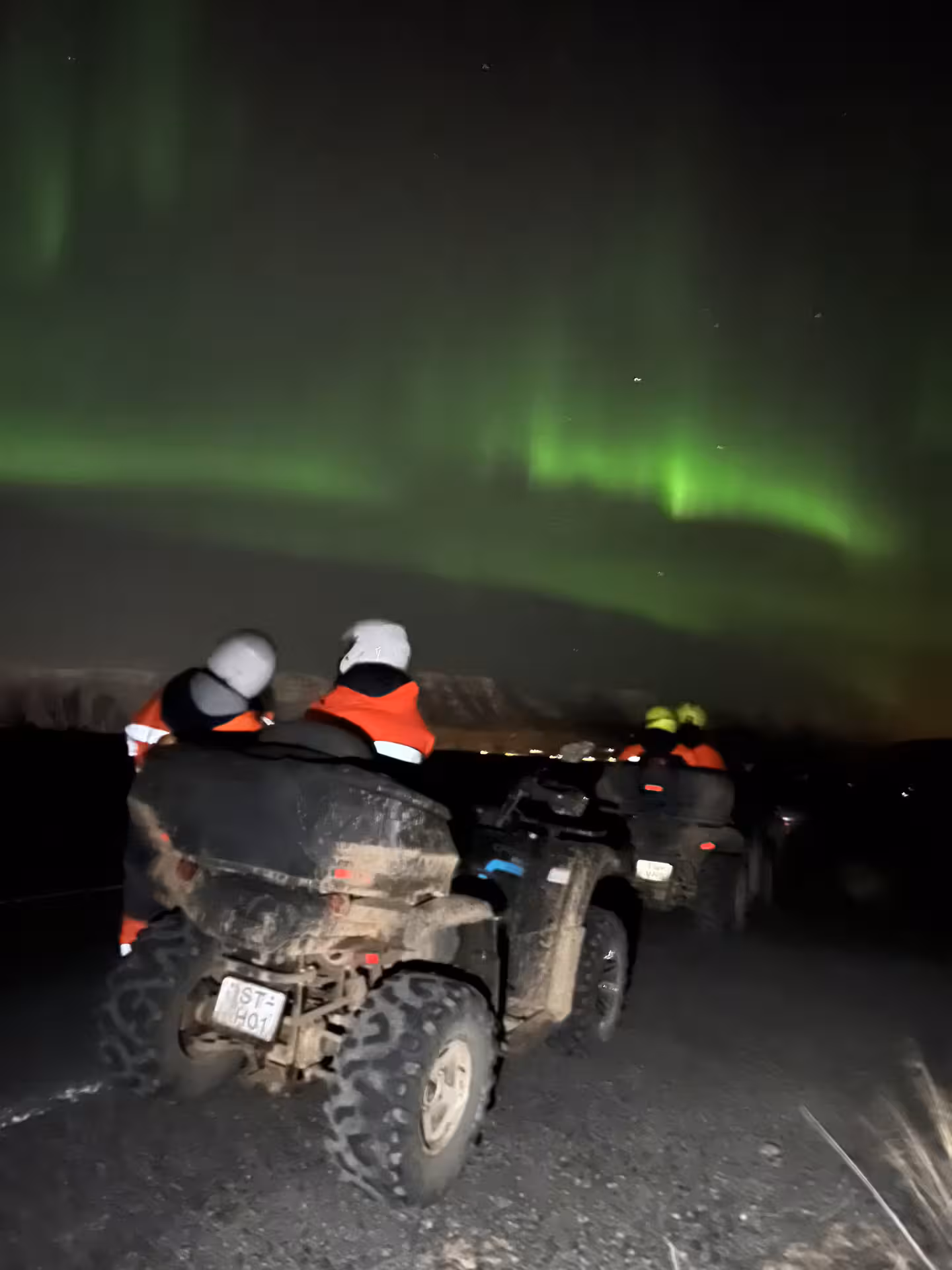 ATV riders in orange vests watching green northern lights aurora borealis in Iceland night sky