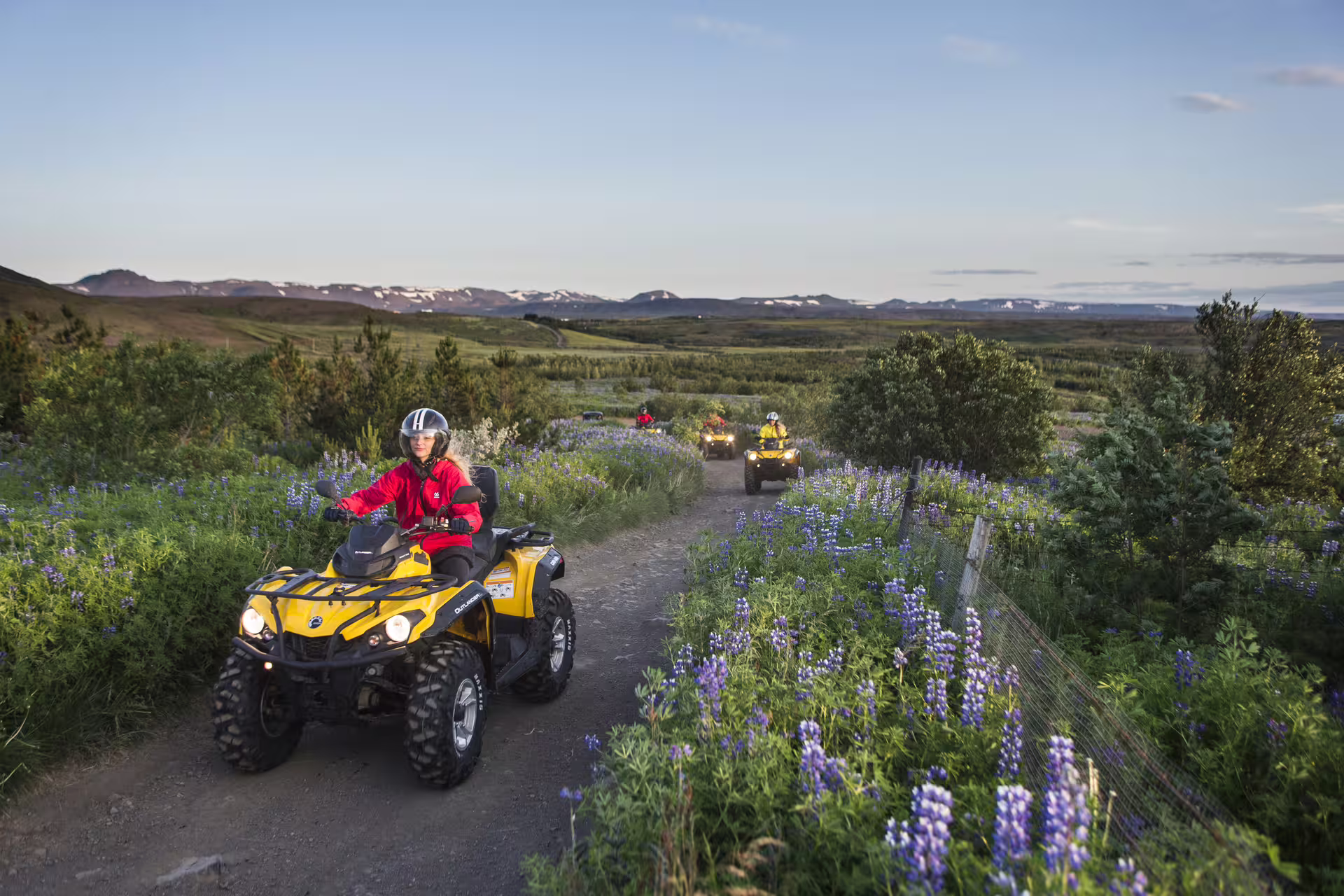 ATV riders explore a scenic trail surrounded by lush greenery and wildflowers, perfect for adventure and caving enthusiasts.