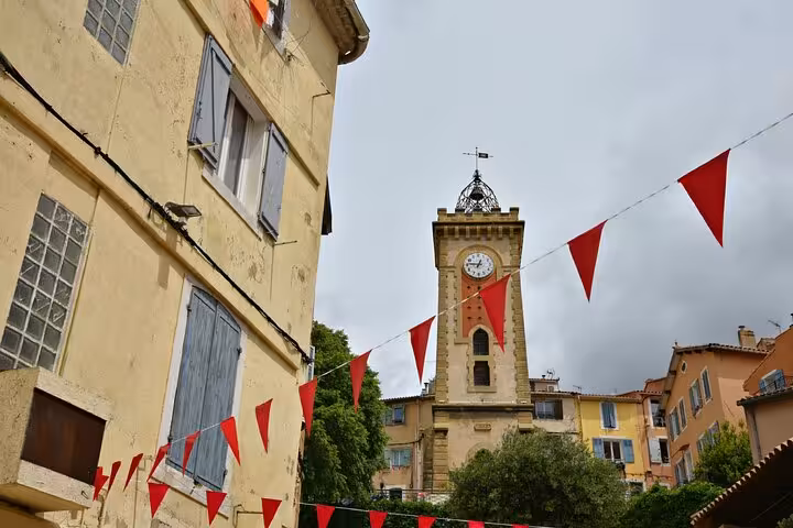 Aubagne clock tower with red bunting flags and historic buildings on a walking tour route