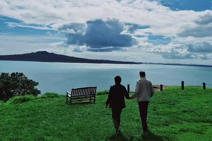 Couple enjoying a walk on a grassy hill with stunning views of Rangitoto Island on an Auckland day tour.