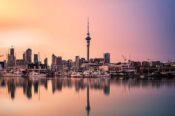 Auckland harbor at sunset with Sky Tower silhouetted against a colorful sky, creating a picturesque waterfront scene.