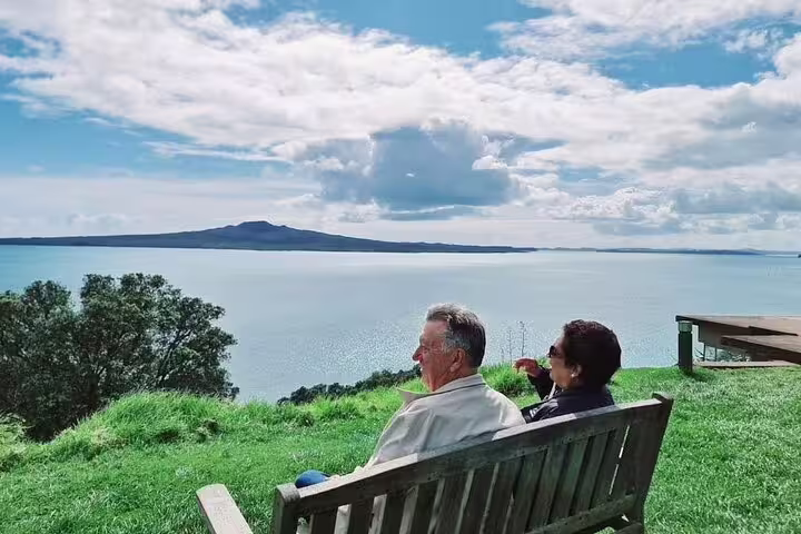 Visitors relaxing on a bench overlooking Rangitoto Island during the Private Auckland Highlight Day Tour.