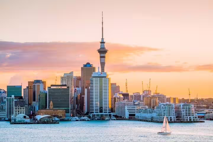 Sailboat gliding past Auckland's iconic skyline at sunset, highlighting the Sky Tower during a private day tour.