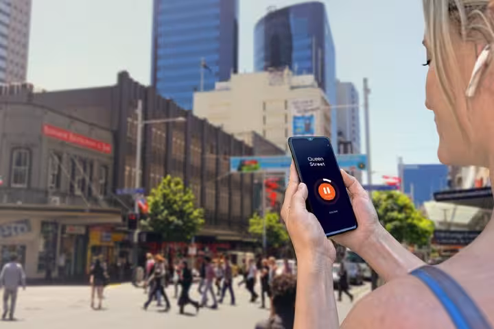 Woman holding smartphone with audio tour app on Queen Street, Auckland city centre