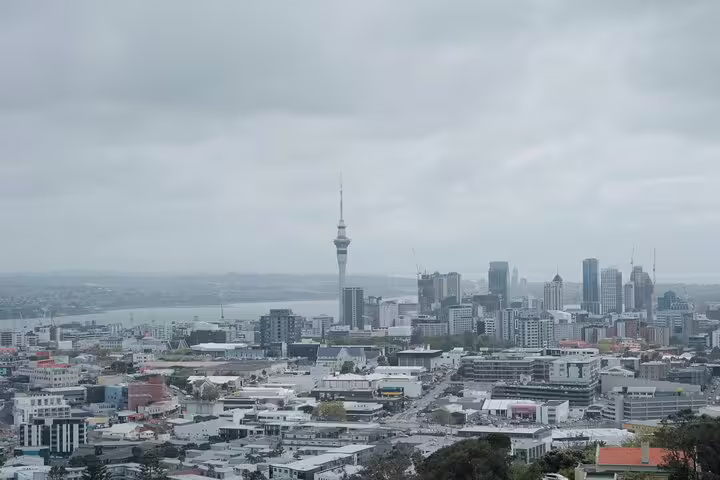 Scenic view of Auckland skyline featuring Sky Tower and urban landscape on a cloudy day.