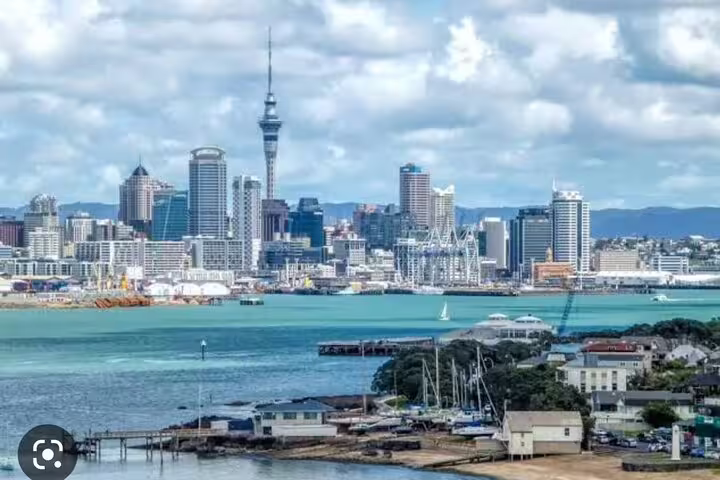 Auckland city skyline with the Sky Tower and vibrant harbor under a partly cloudy sky.