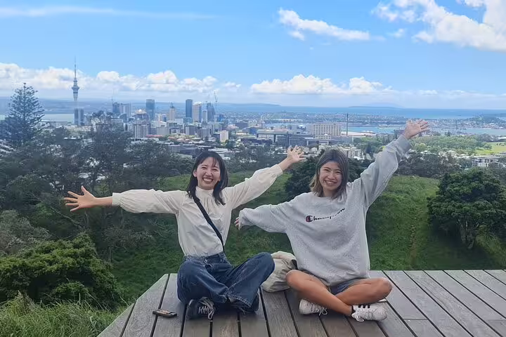Two smiling tourists enjoy the breathtaking Auckland skyline from a scenic viewpoint.
