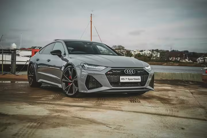 Gray Audi RS7 Sportback luxury sedan parked near waterfront on overcast day