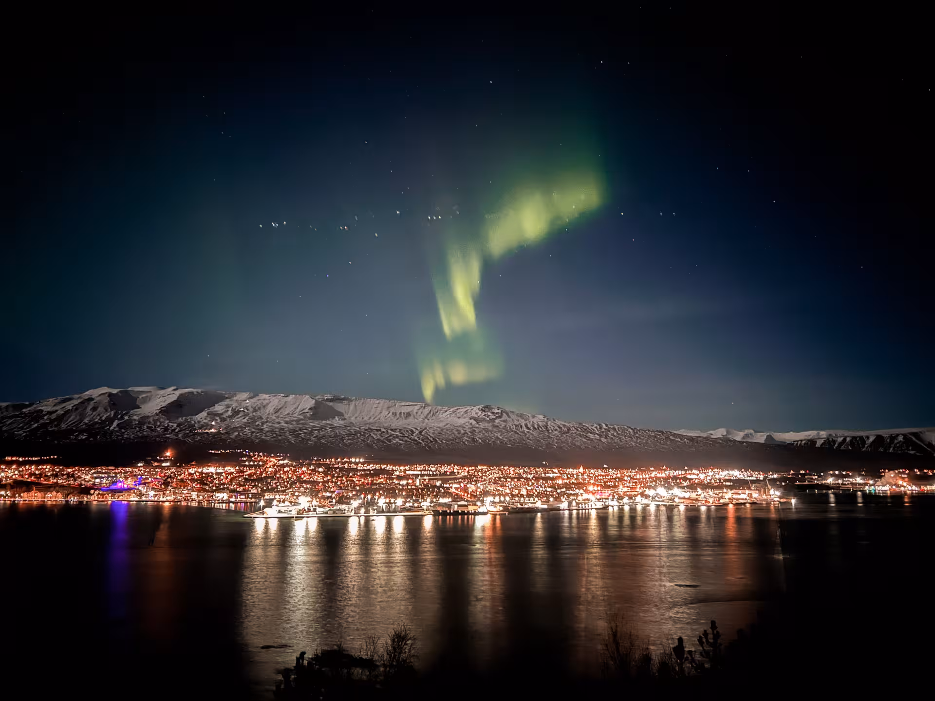 Northern Lights over Arctic fjord town and snowy mountains, perfect Aurora Borealis tour night view