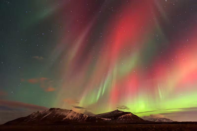 Breathtaking red and green aurora borealis illuminating snowy Iceland mountains on a hidden fjord night tour