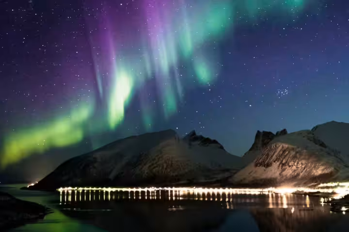 Breathtaking purple and green aurora borealis over snow-capped Norwegian fjord mountains on an exclusive northern lights luxury Arctic cruise