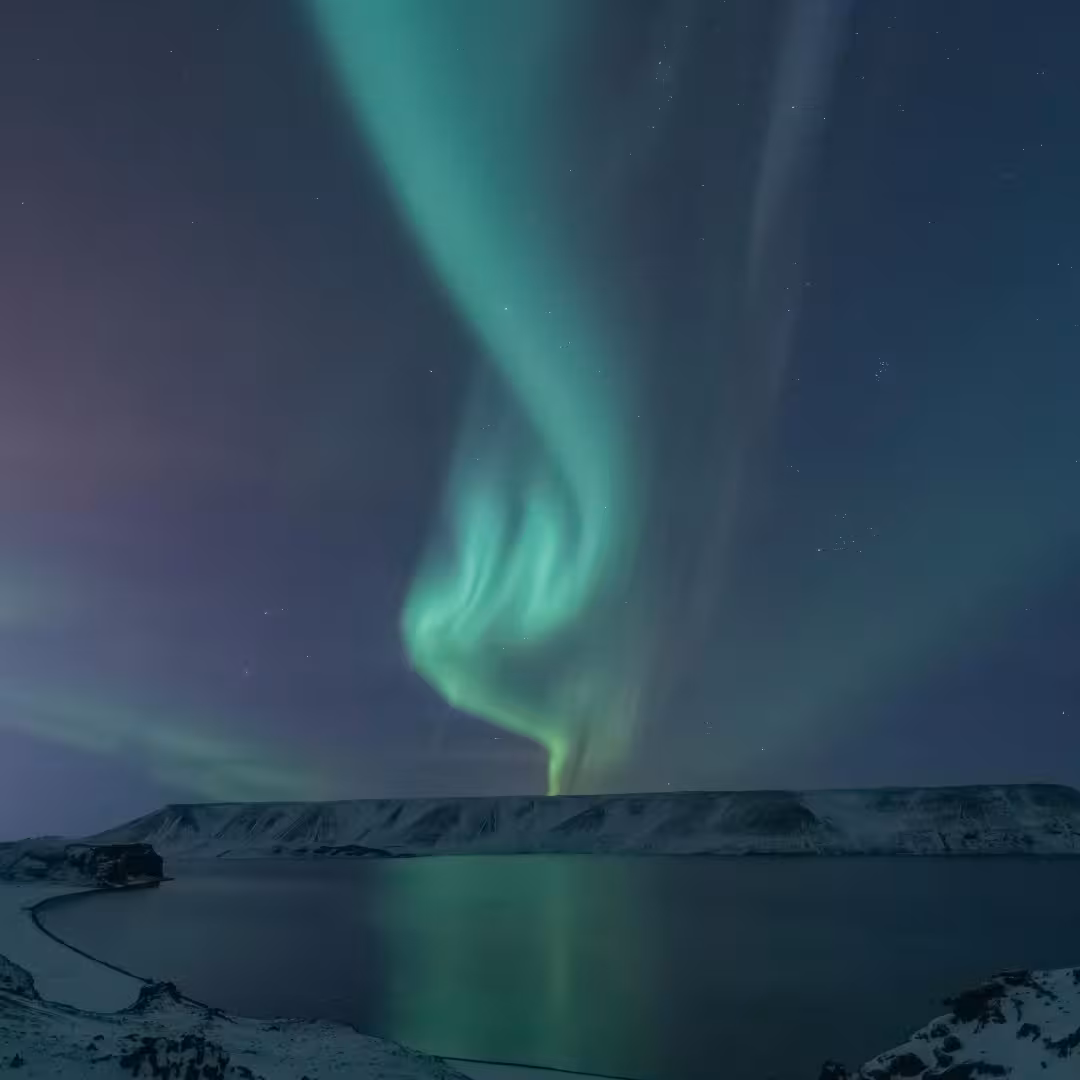 Breathtaking green aurora borealis swirling over a snowy Arctic fjord on a premium Northern Lights luxury cruise