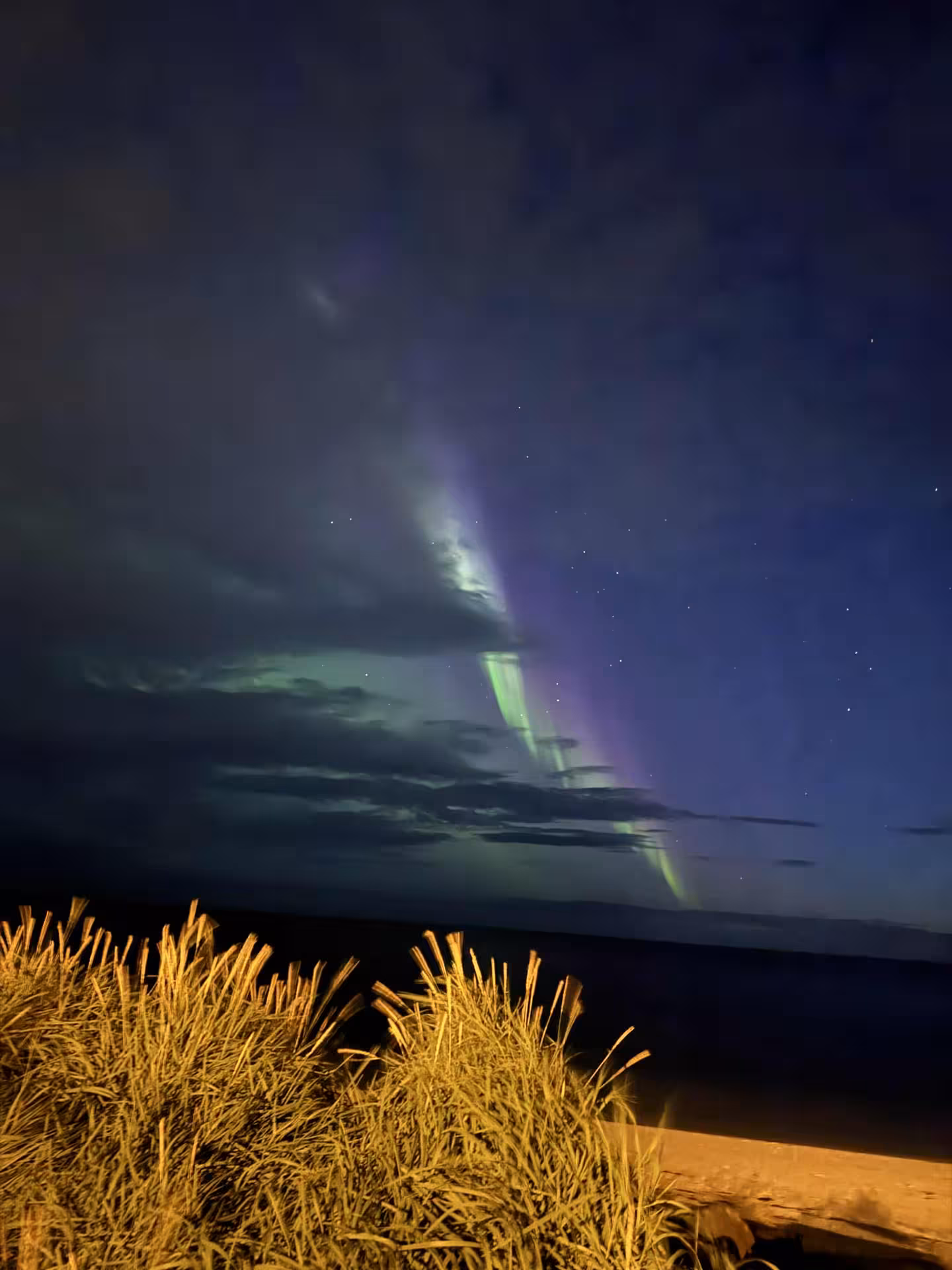 Northern lights beam with purple glow above clouds and tundra, perfect aurora borealis viewing tour