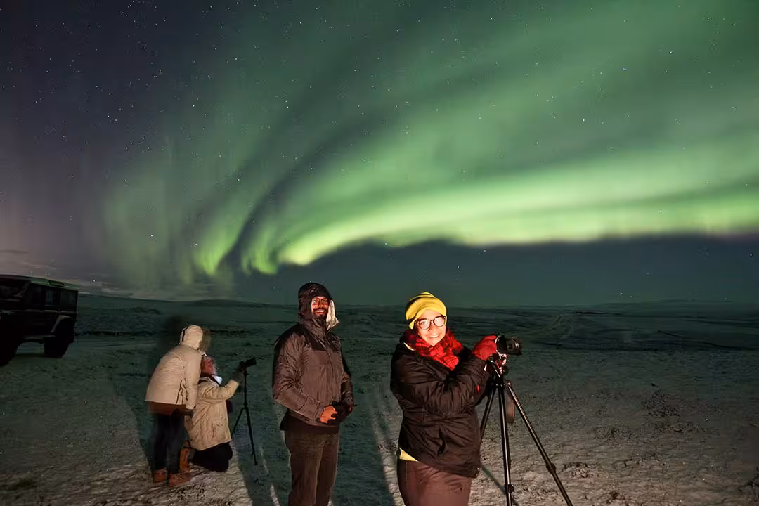 Aurora borealis tour with photographers on snowy tundra, capturing northern lights and stars on tripods