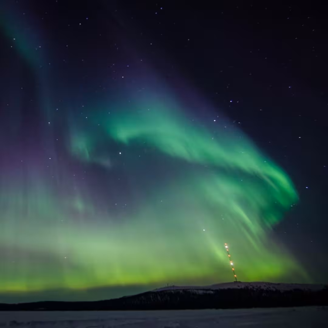 Vivid green and purple aurora borealis swirling over snowy Arctic landscape on exclusive northern lights luxury cruise